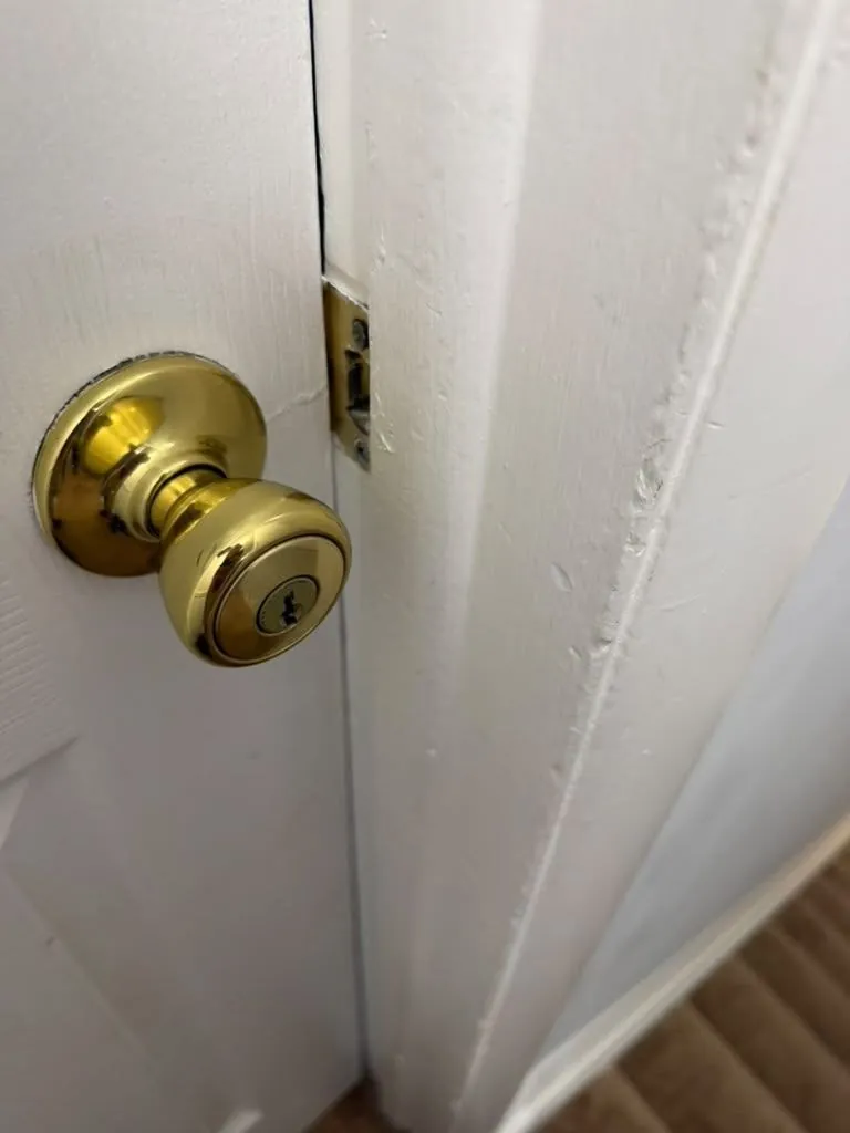 Brass knob lock on a white interior door, with the latch and strike visible.