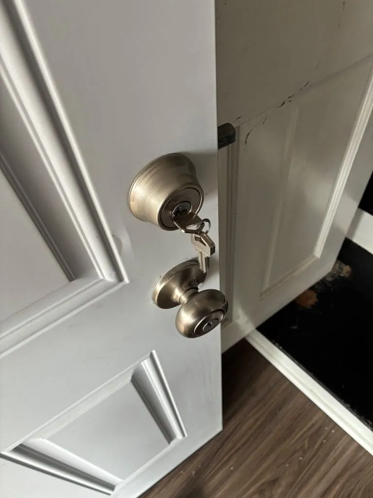 Deadbolt and knob on a white door, with the keys still in the lock.