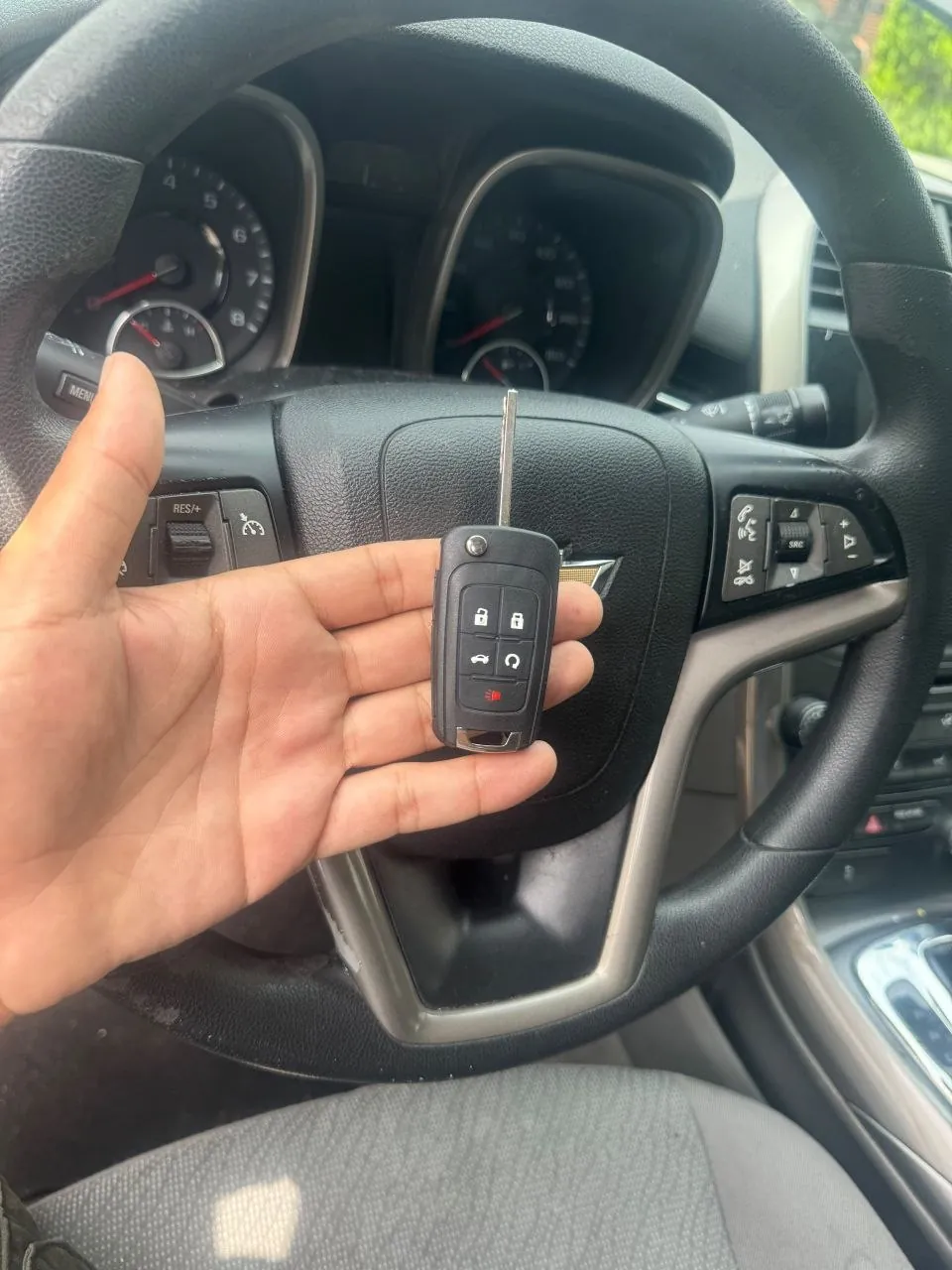 Hand holding a flip key in front of a car steering wheel.