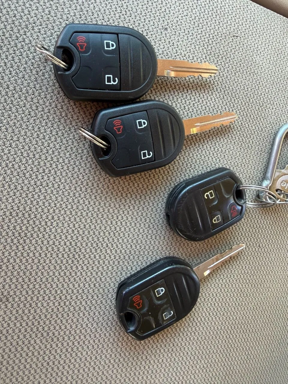 Four flip-style car keys with remote buttons on a car seat.