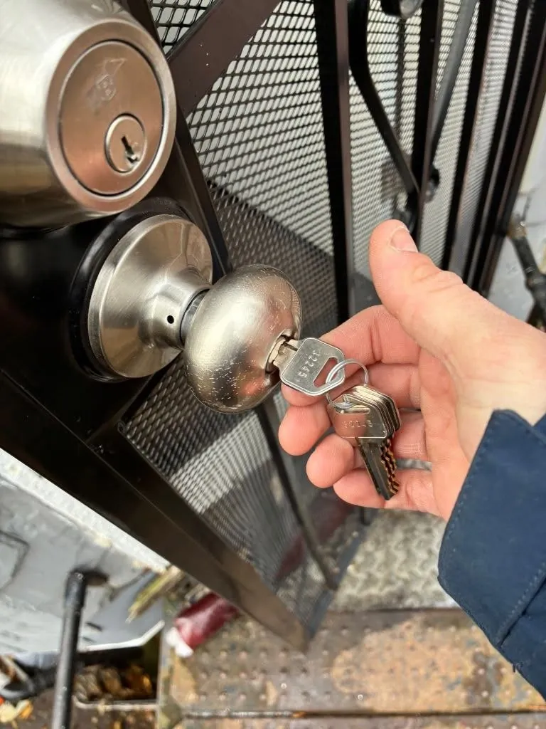 Hand turning a key in a knob lock on a security screen door.