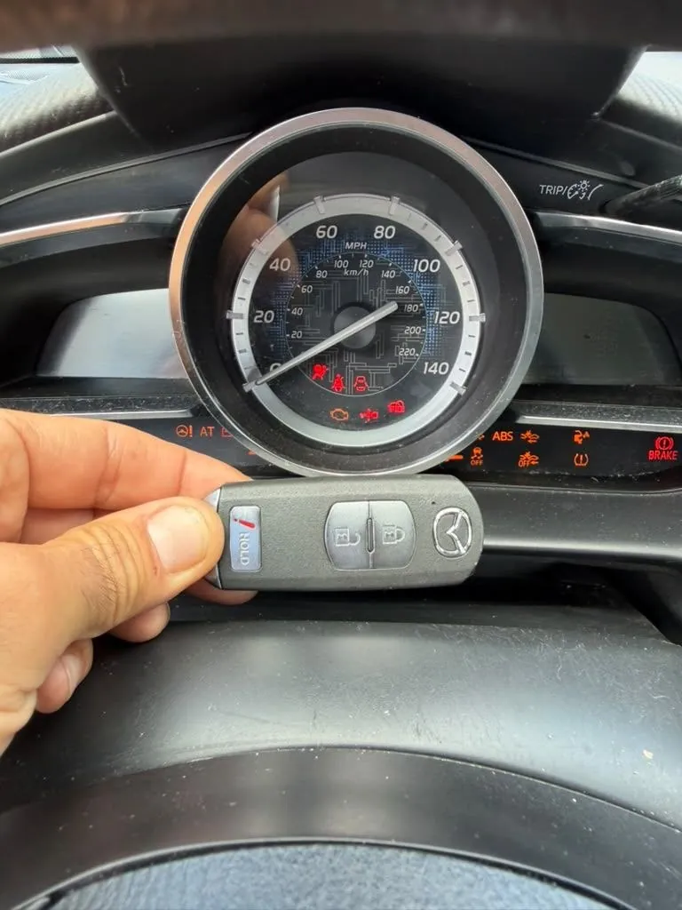 Hand holding a smart key in front of a car dashboard.