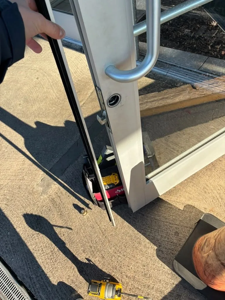 Glass storefront door held open during work, with tools on the pavement.