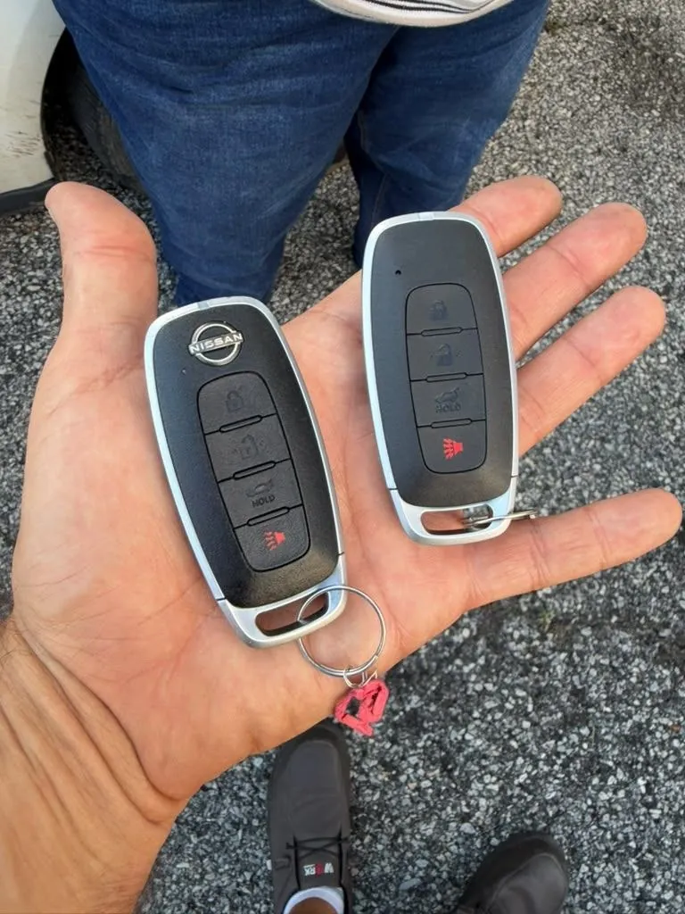 Hand holding two smart key fobs outside a car.
